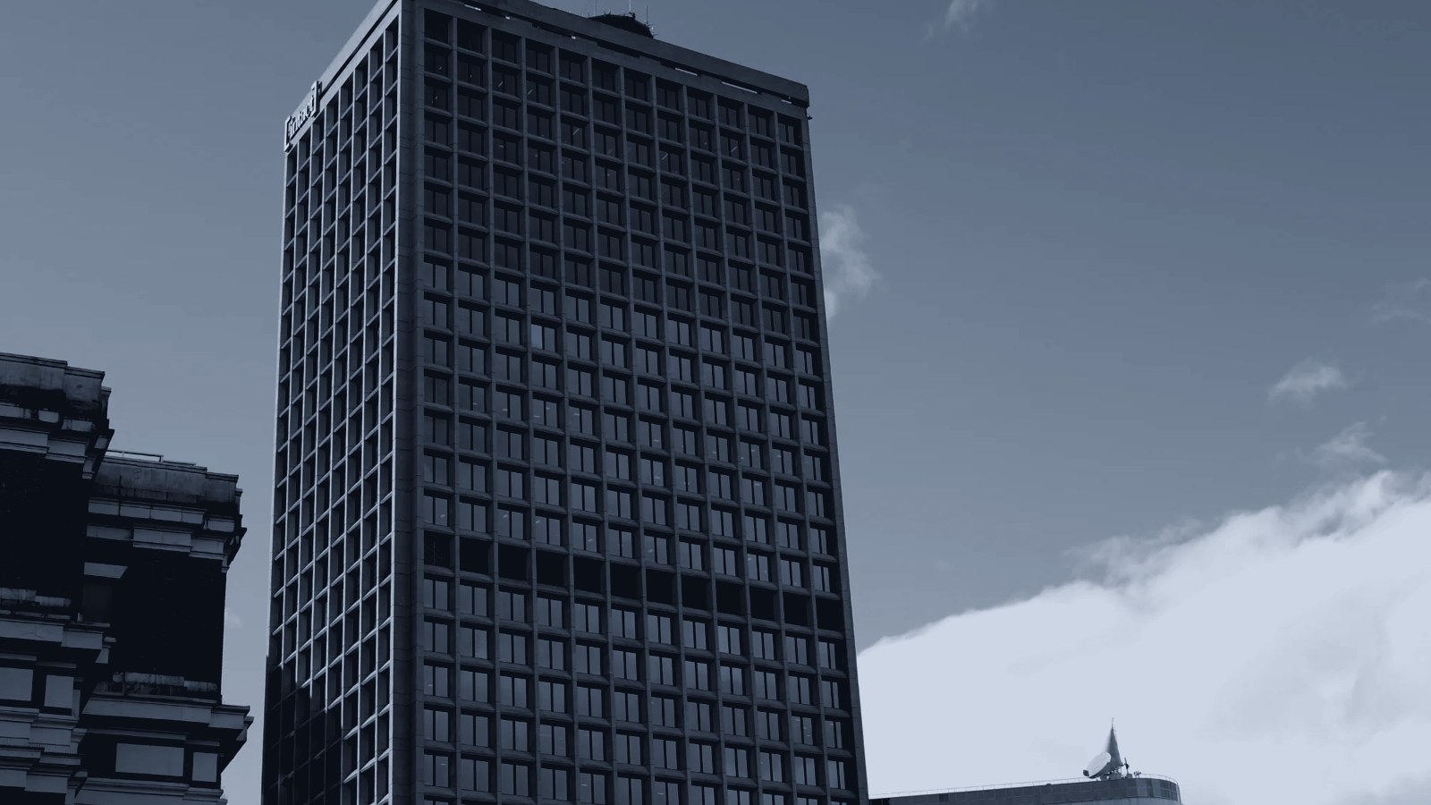 A grid-windowed office tower under a stormy sky, in silver-blue duotone